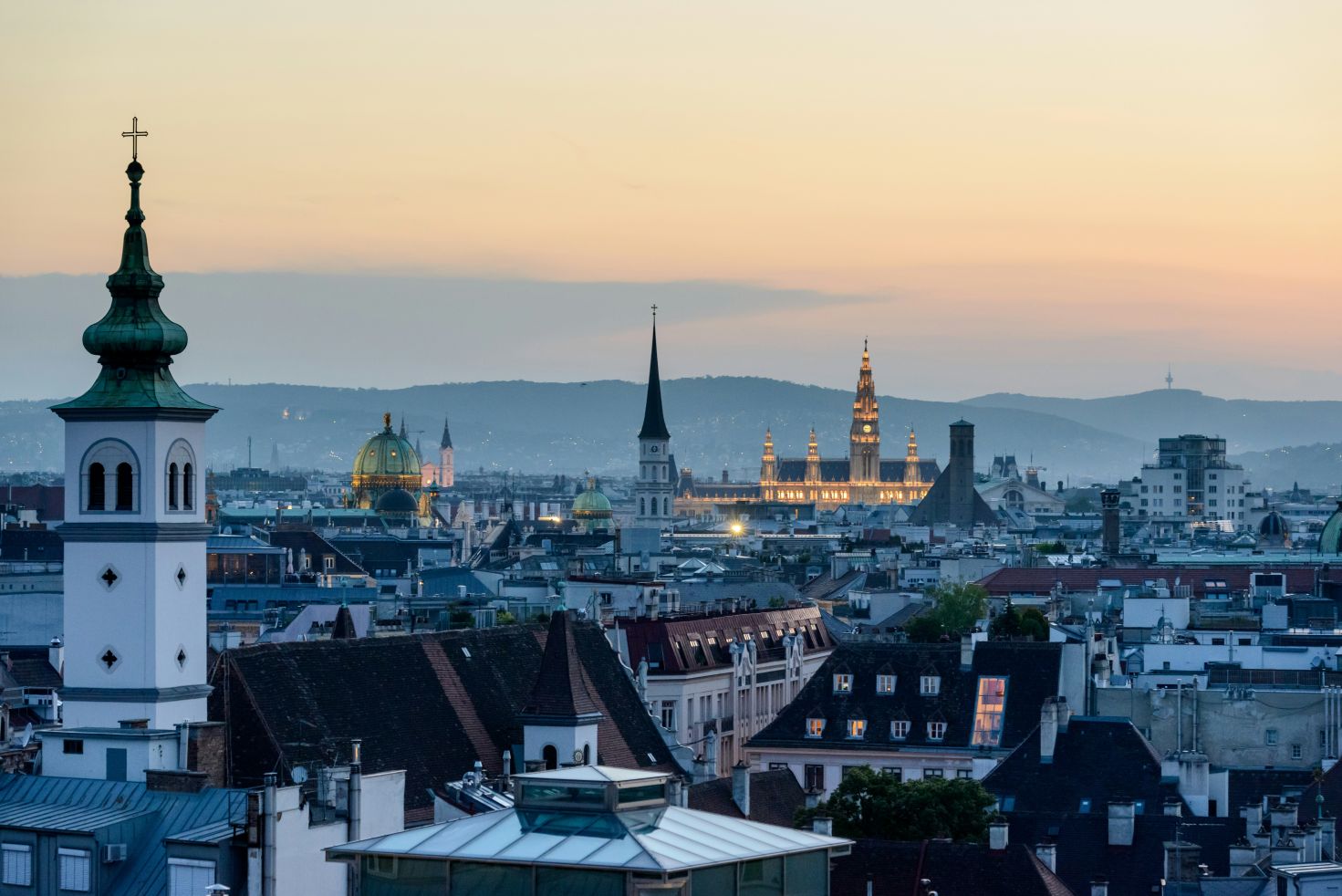Abendliches Panorama der Wiener Altstadt, Kircht&uuml;rme und das beleuchtete Rathaus im Hintergrund.