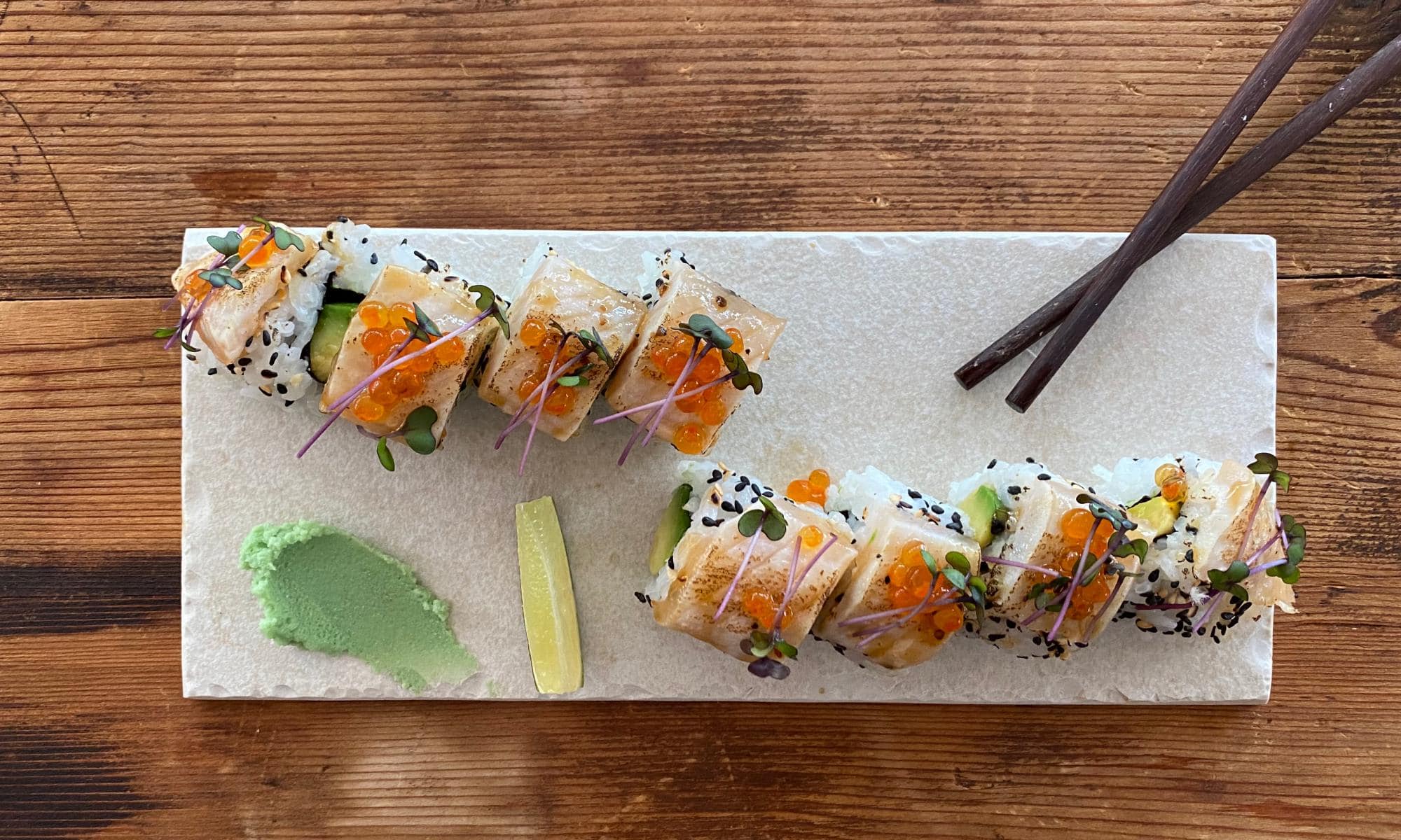 Eine kunstvoll angerichtete Sushi-Platte mit flambiertem Fisch, Lachsrogen und frischen Kr&auml;utern auf einem rustikalen Holztisch.