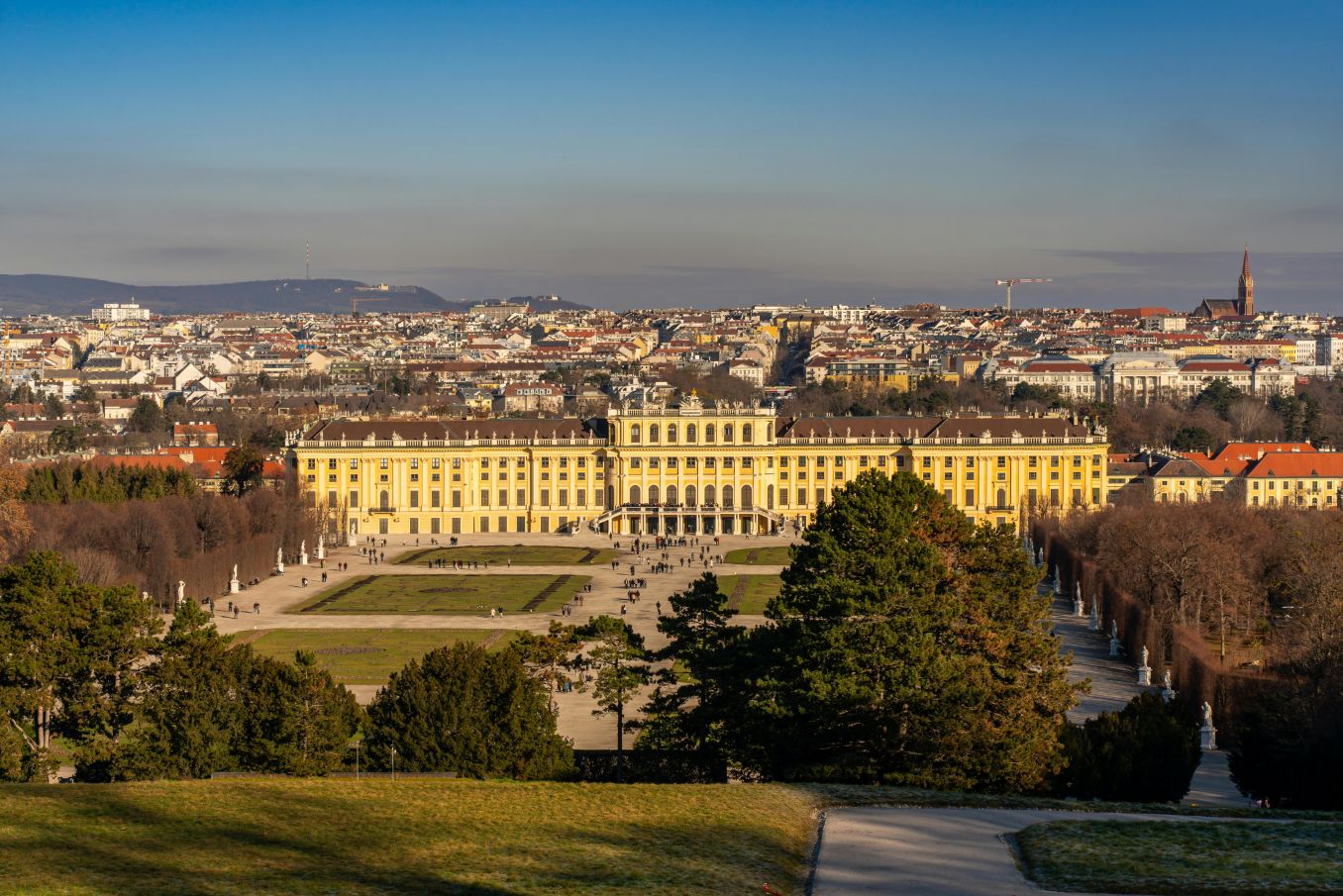 Schloss Sch&ouml;nbrunn in Wien, von der Gartenansicht aus gesehen, umgeben von gr&uuml;nen Parkanlagen und der Stadt im Hintergrund.