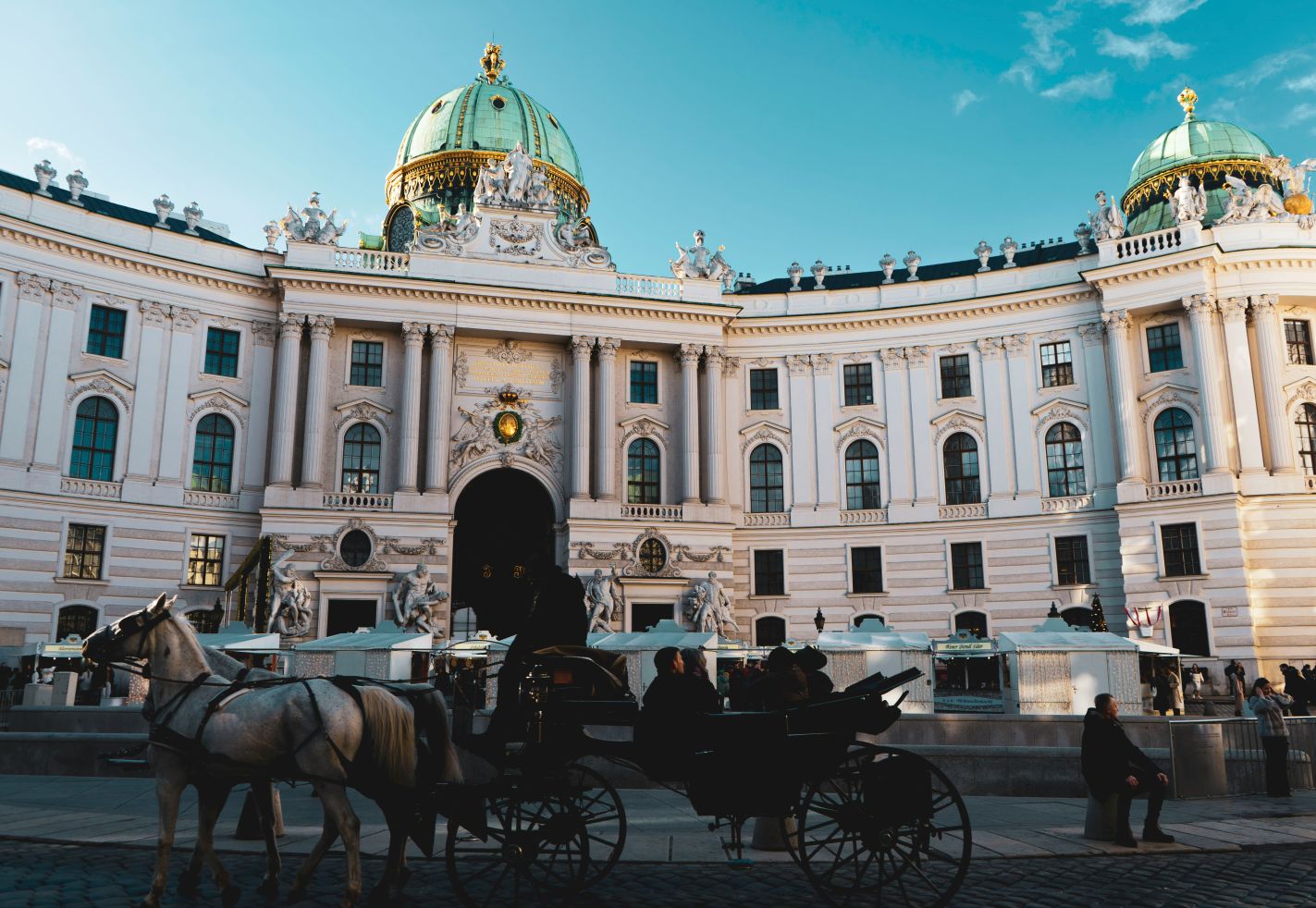Hofburg Wien bei Tageslicht, im Vordergrund eine Pferdekutsche mit zwei wei&szlig;en Pferden, barocke Architektur im Hintergrund.