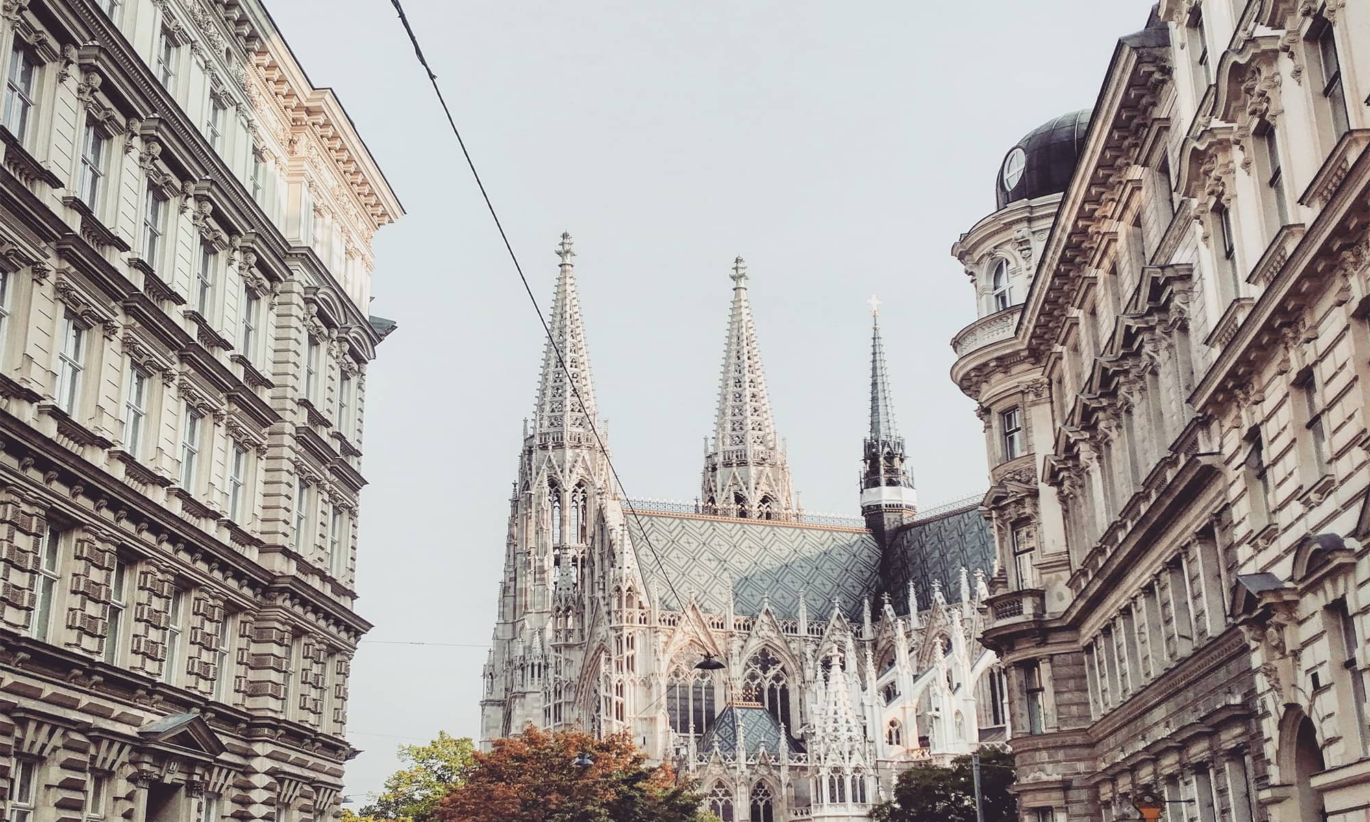 Das Bild zeigt die Votivkirche in Wien, deren neugotische T&uuml;rme im Mittelpunkt stehen.