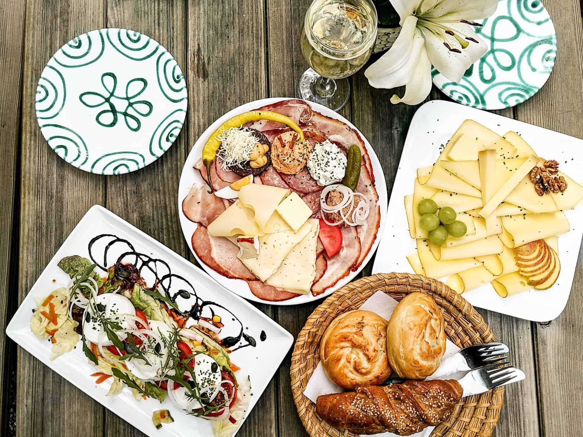 Tisch mit traditioneller &ouml;sterreichischer Jause, bestehend aus K&auml;se, Aufschnitt, Geb&auml;ck und Salat, serviert bei einem Heurigen.