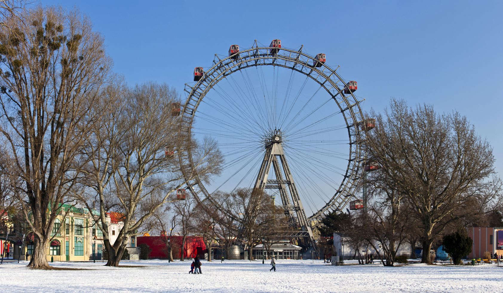 Das Wiener Riesenrad im Prater bei winterlichem Wetter, mit schneebedecktem Boden und kahlen B&auml;umen im Vordergrund.