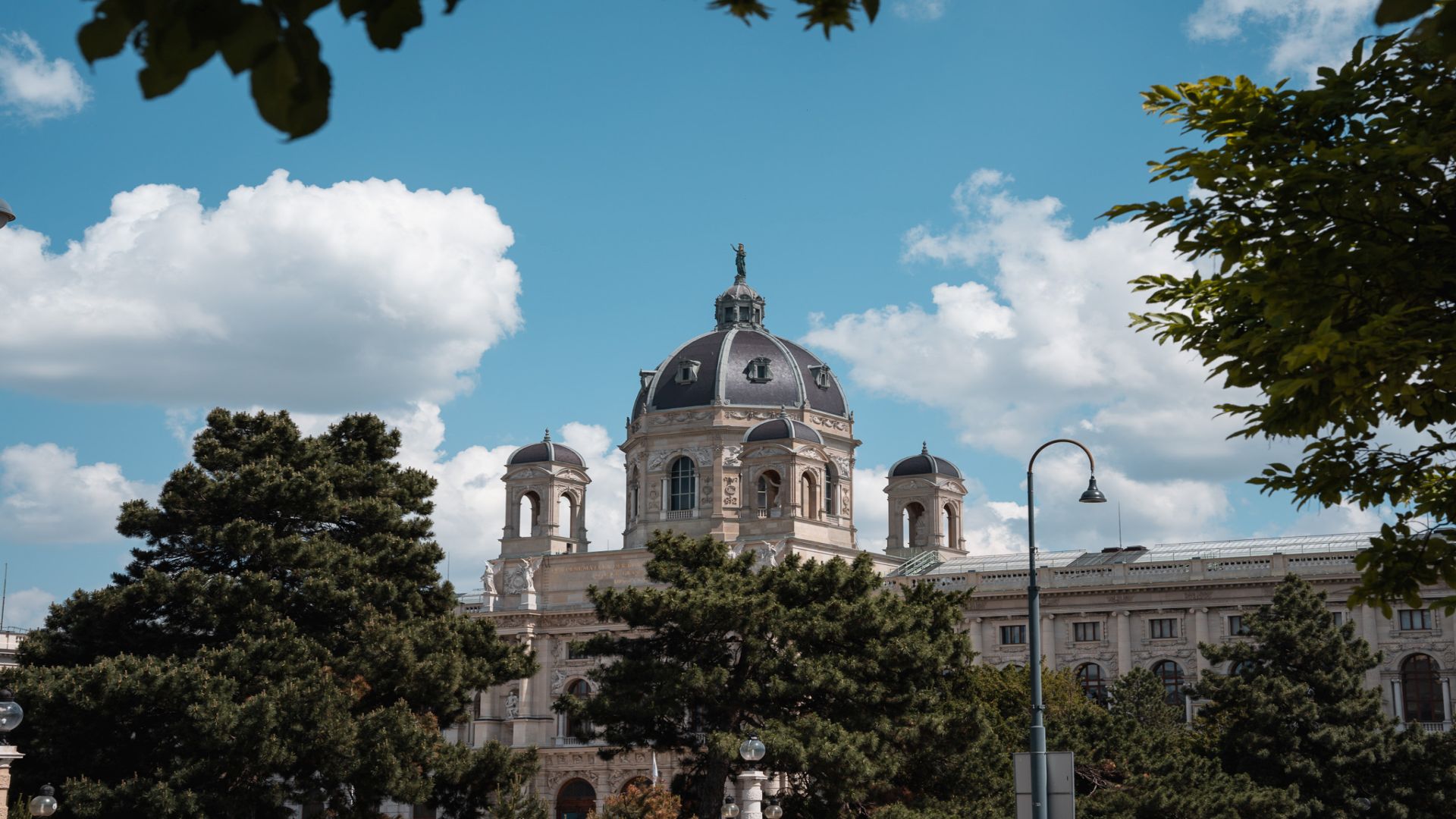 Au&szlig;enansicht des Kunsthistorischen Museums in Wien, umrahmt von gr&uuml;nen B&auml;umen und mit blauem Himmel im Hintergrund.